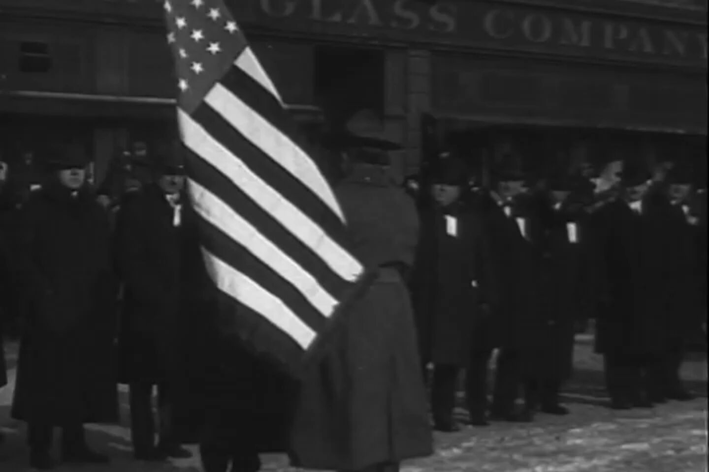 A flag bearer and a crowd of men in coats at a Liberty Bond parade in Detroit, 1918.